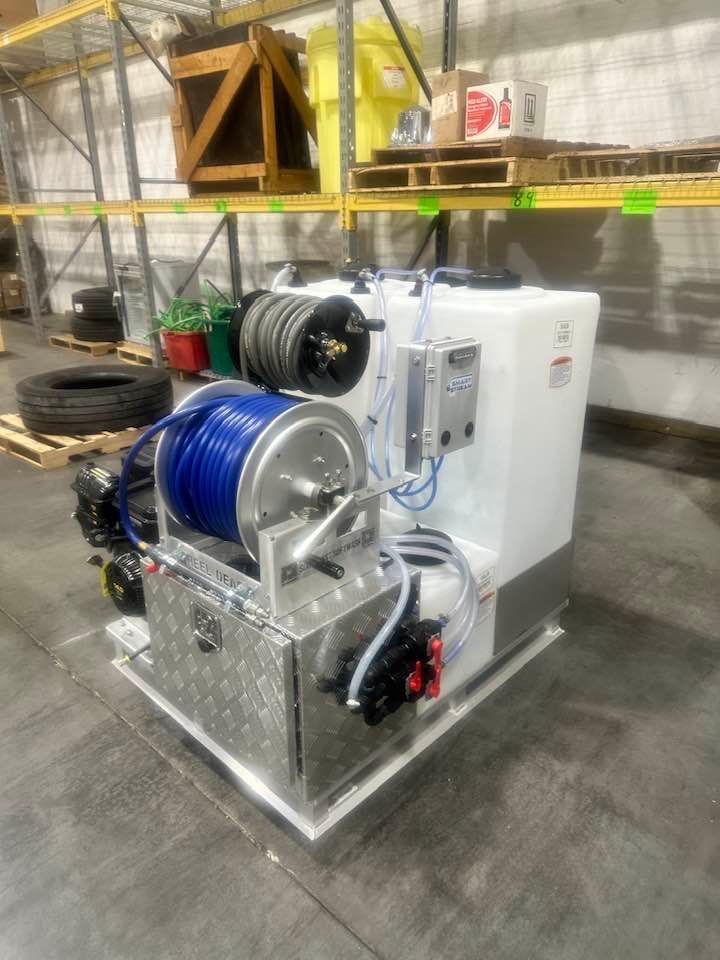 Industrial hose reel machine with blue hose and white tank on a metal frame in a warehouse.