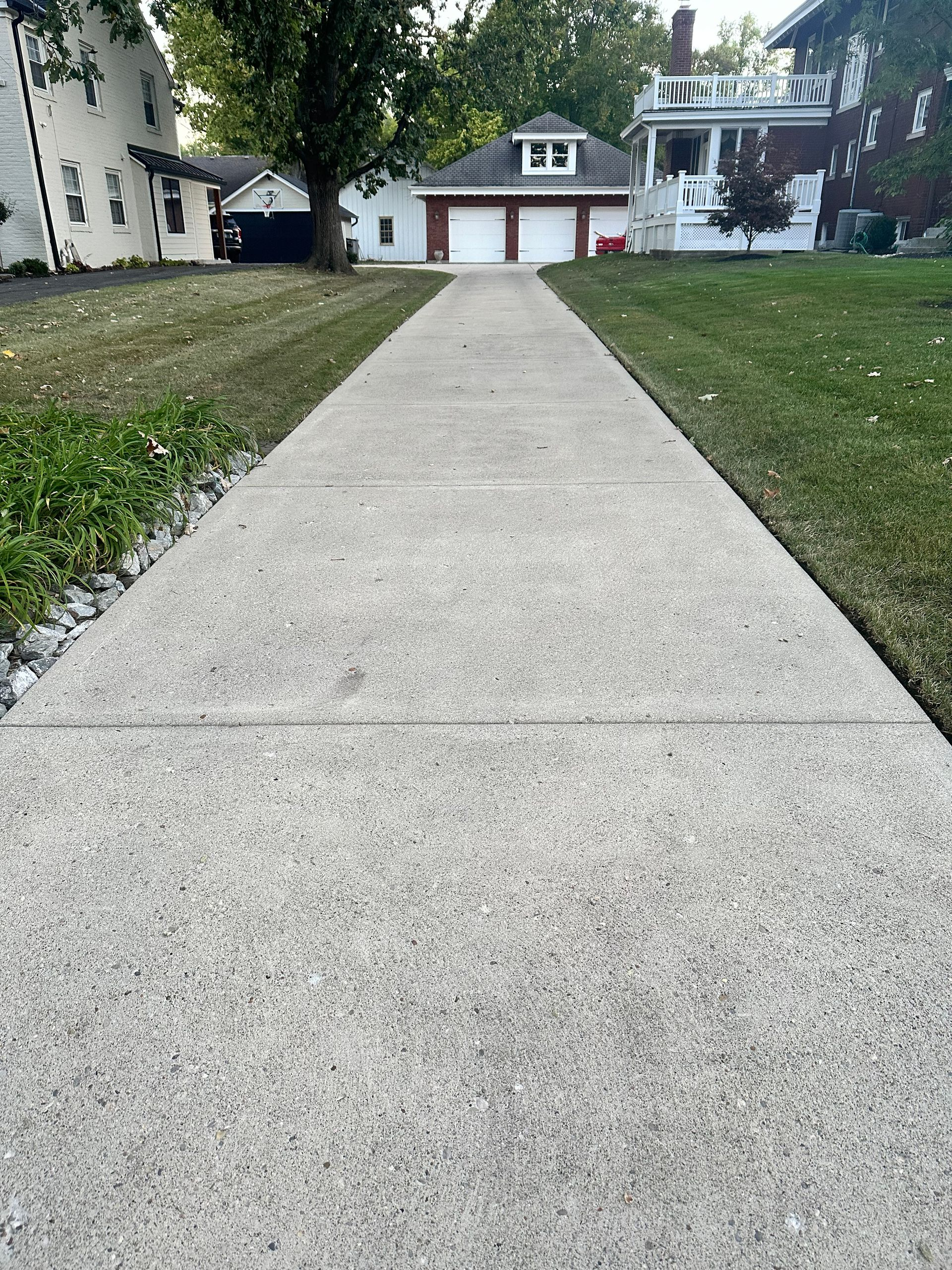 Concrete driveway leading to a two-story house with a red garage door and trees on either side.