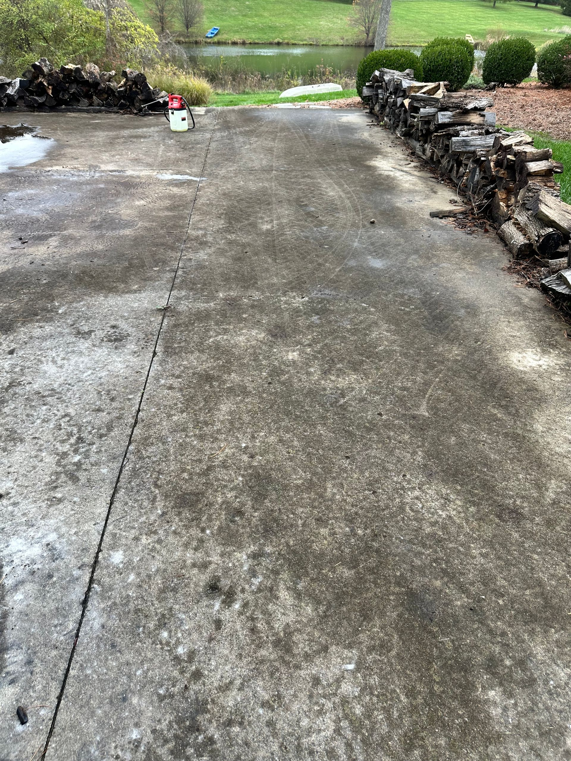 Wet concrete driveway bordered by stone walls, leading to a green yard.