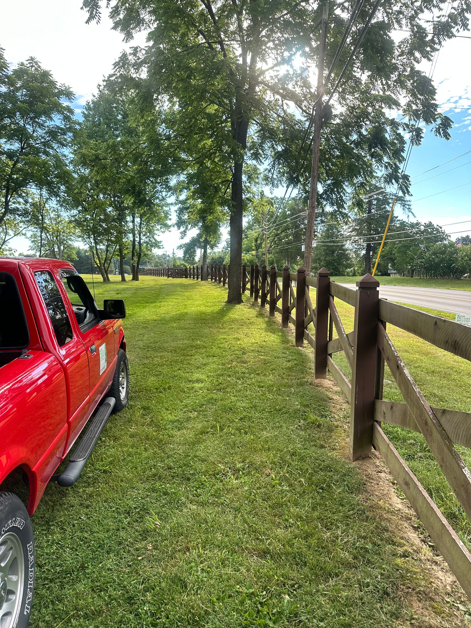 Red pickup truck beside a grassy fence line in a sunny rural field.