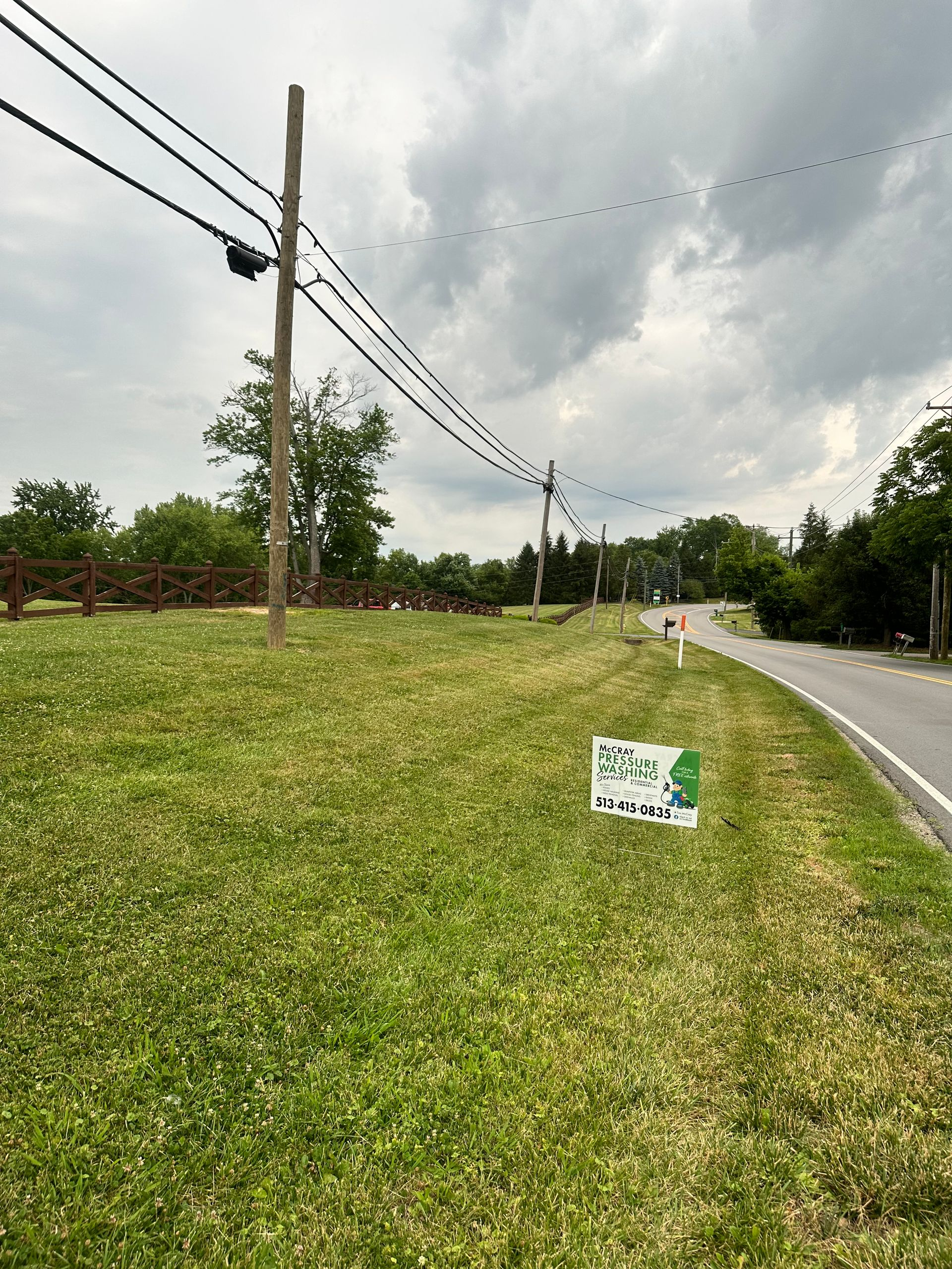 Grassy roadside with utility poles, cloudy sky, and a small sign beside a curving paved road