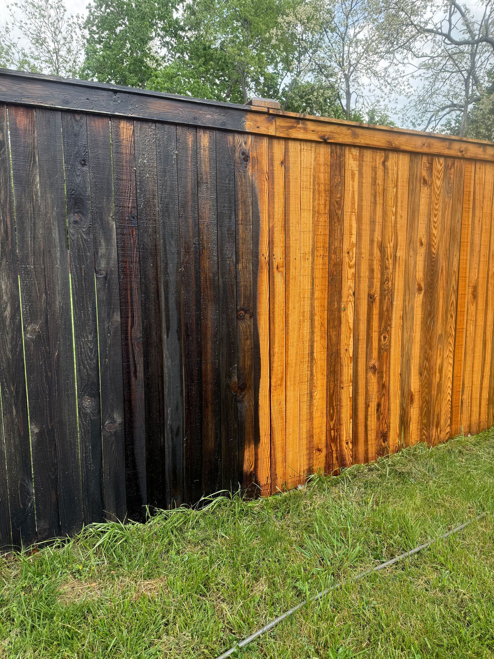 Weathered wooden fence with black, gray, and orange stained boards beside a grassy yard.