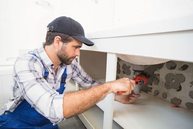 Plumber using a red drill to install pipes inside a wall cavity
