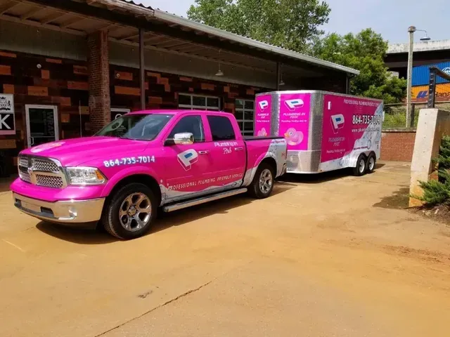 Pink pickup truck towing a pink trailer parked beside a building