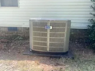 Outdoor air conditioner unit beside a house with beige siding and brick foundation