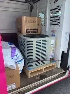 Boxes and a large HVAC unit strapped on a wooden pallet inside a moving truck