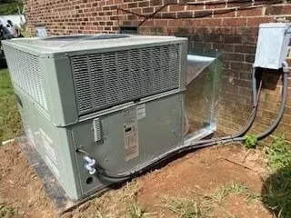 Outdoor HVAC unit beside a brick wall with connected metal ductwork and electrical conduit