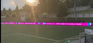 Sunset over a sports field with bright magenta digital signage along the sideline and empty bleachers nearby