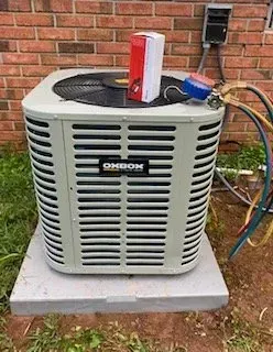 Outdoor HVAC unit beside a brick wall with gauges and hoses attached to the top