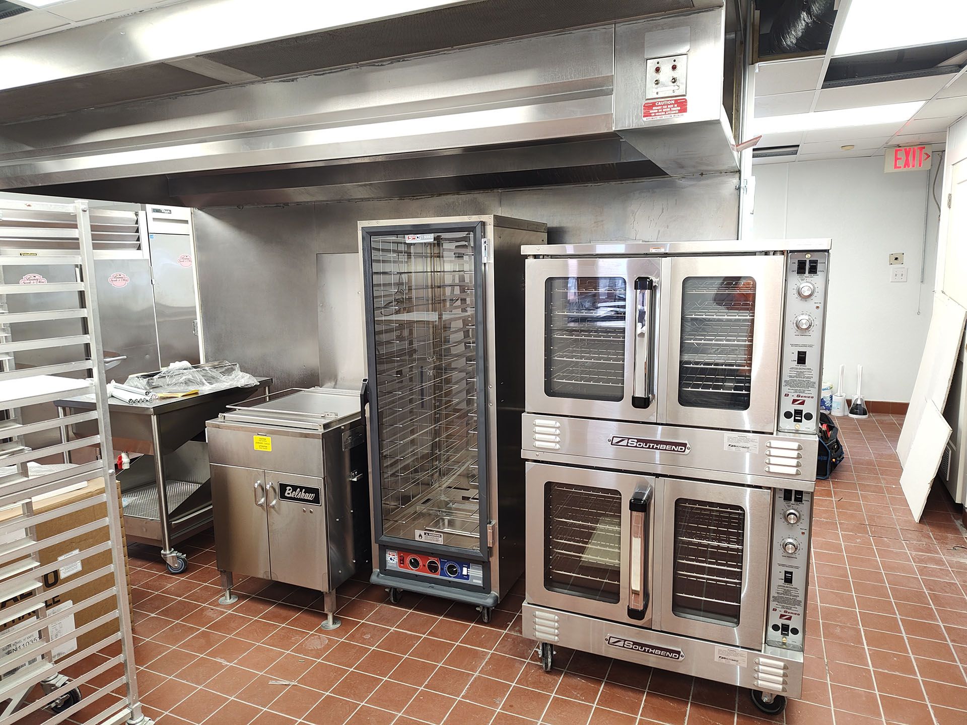 A kitchen with a lot of stainless steel appliances and a red tile floor.