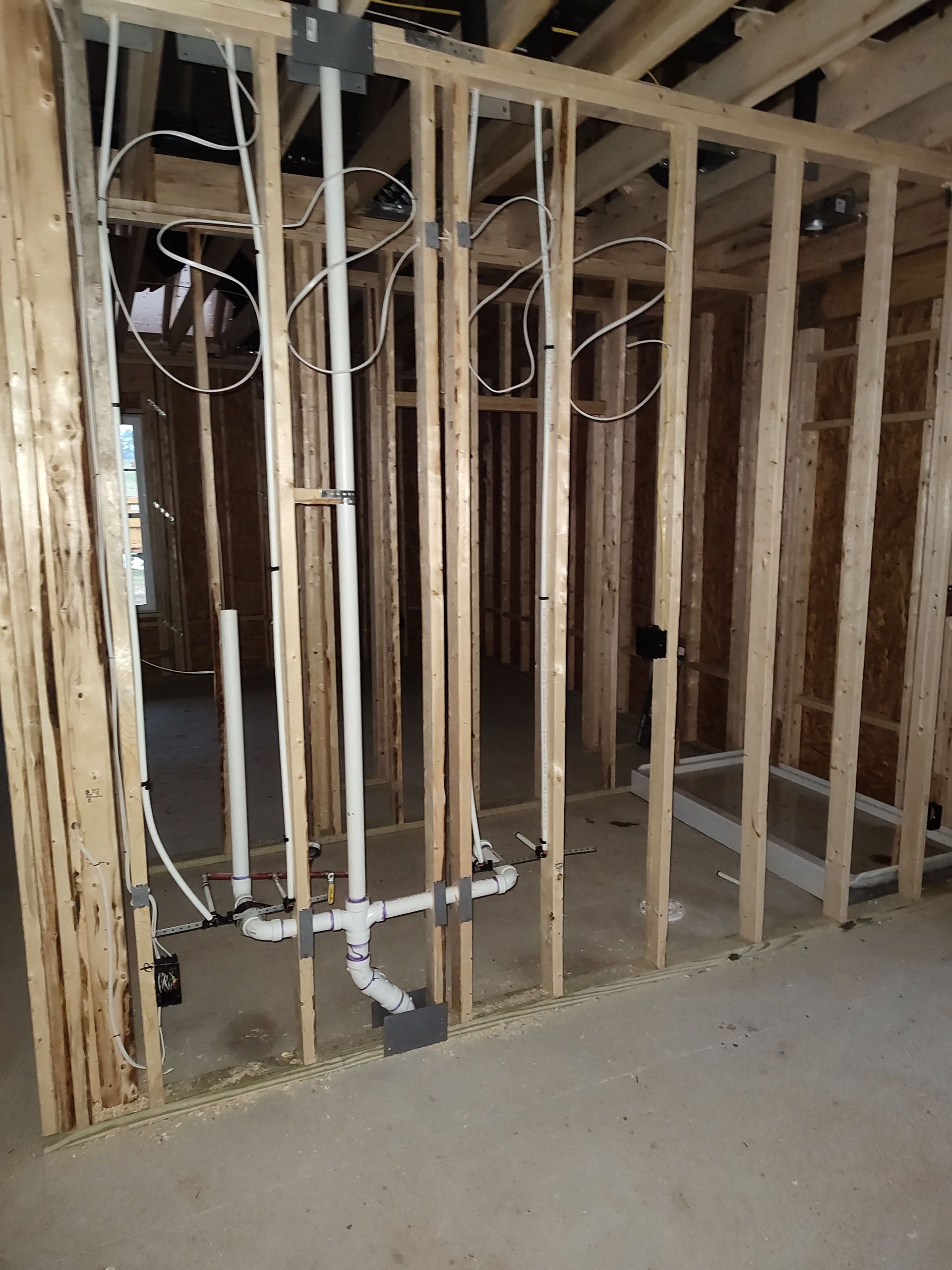 A room in a house under construction with pipes and wires hanging from the ceiling.