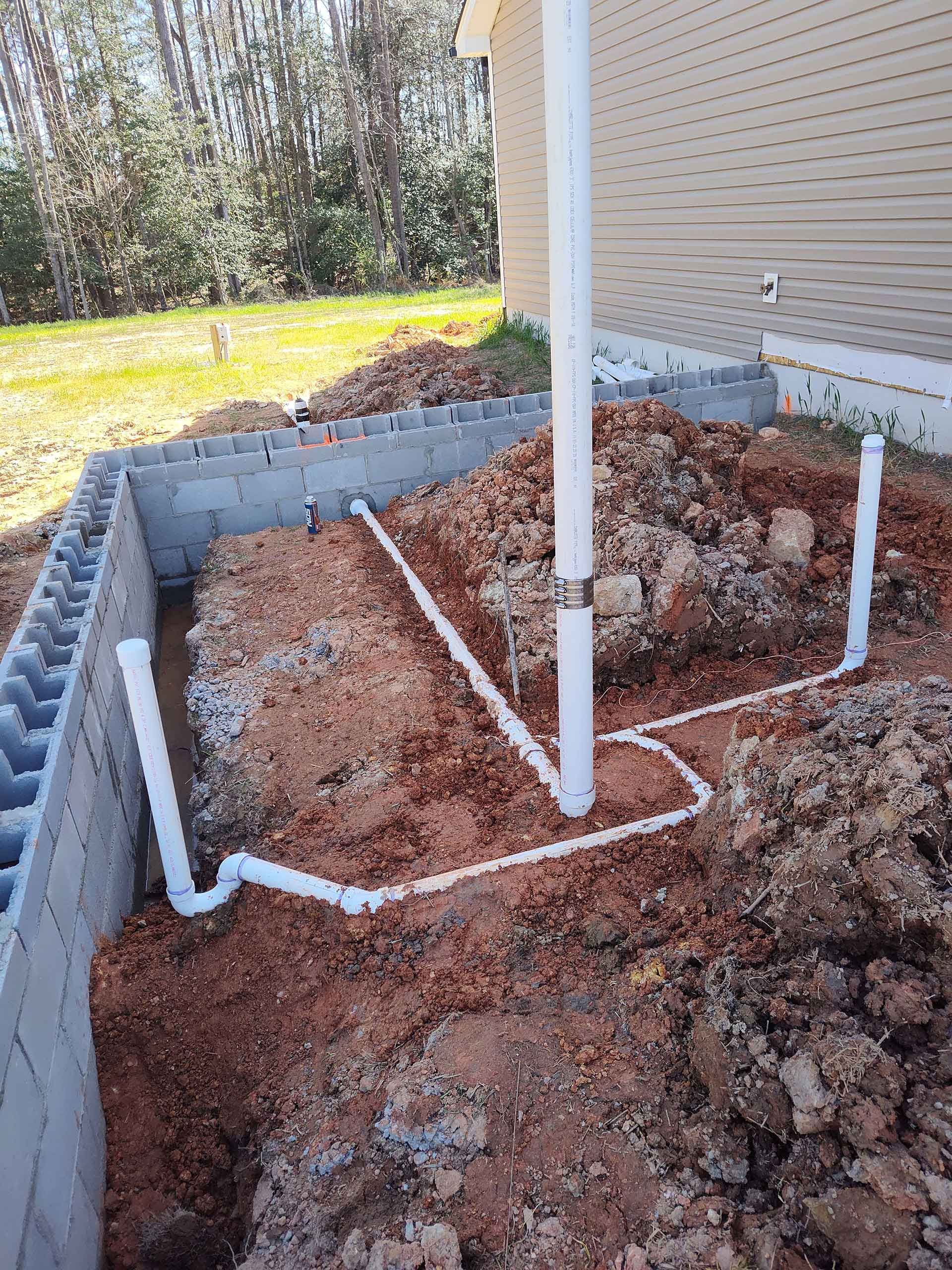 A bunch of pipes are laying in the dirt in front of a house.