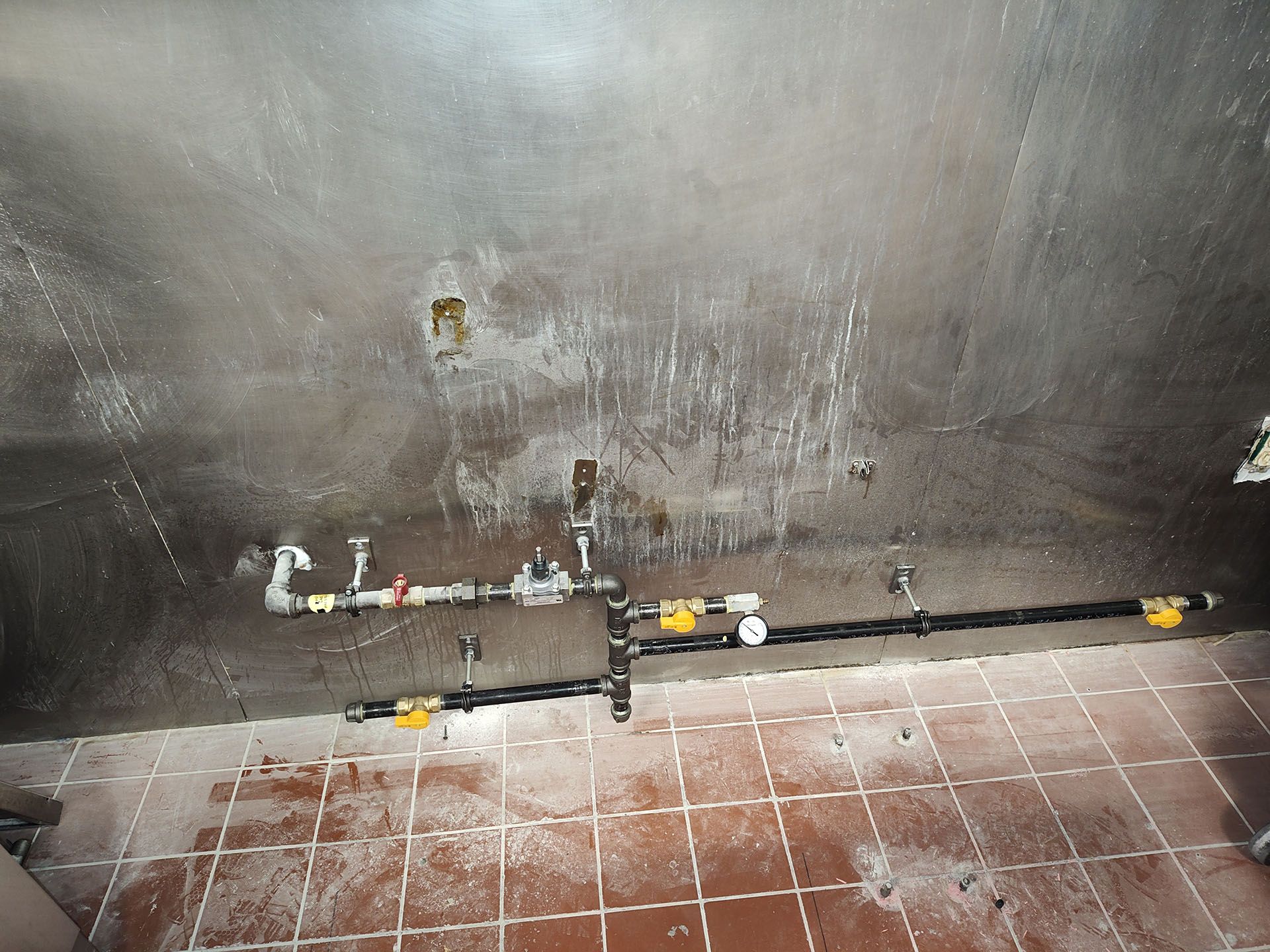 A dirty bathroom with a stainless steel wall and tile floor