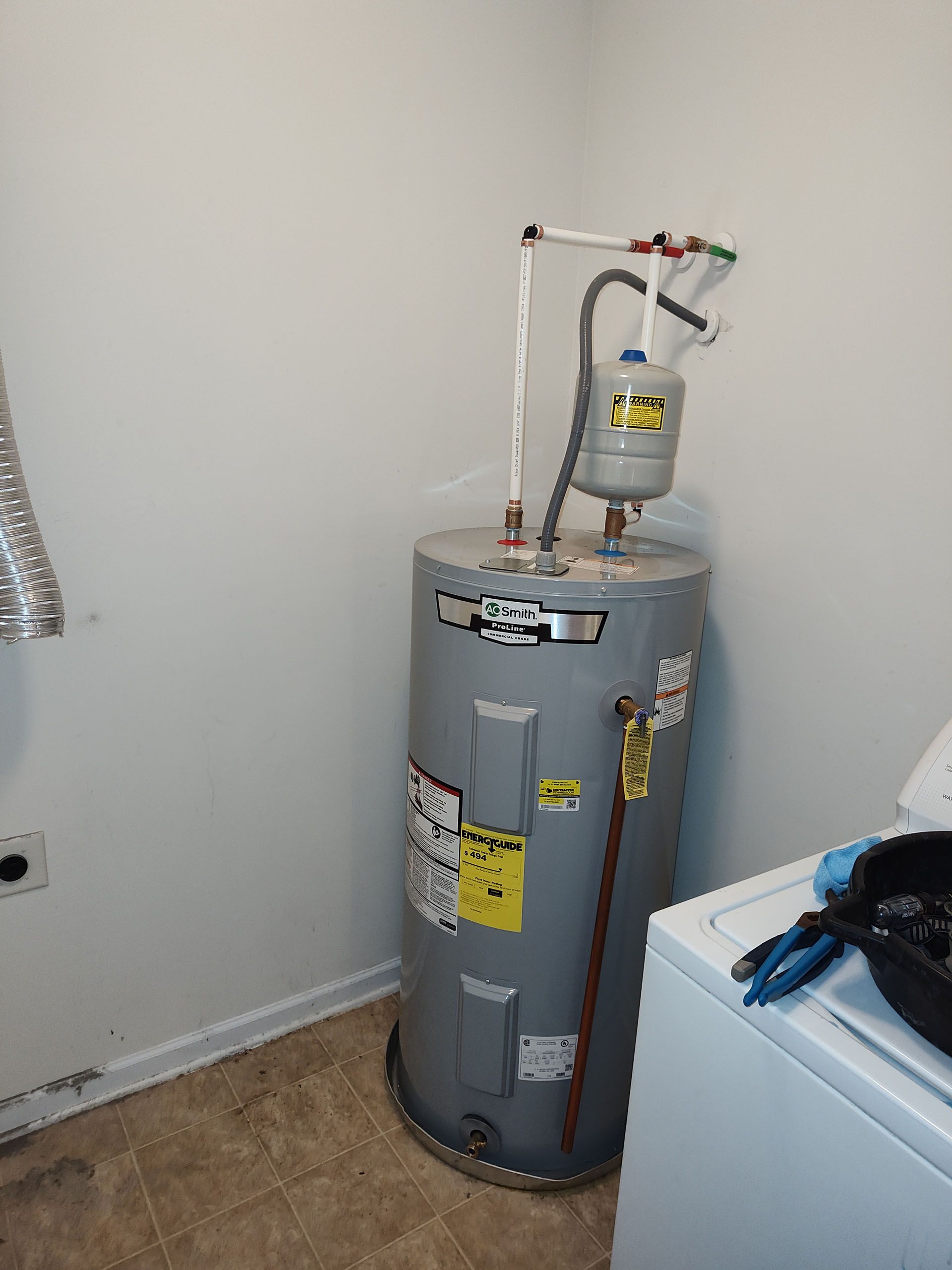 A water heater is sitting in a laundry room next to a washer and dryer.