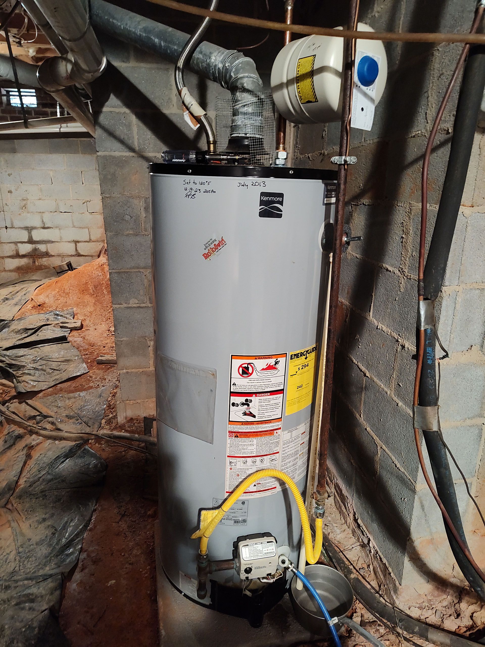 A gas water heater is sitting in a basement next to a brick wall.