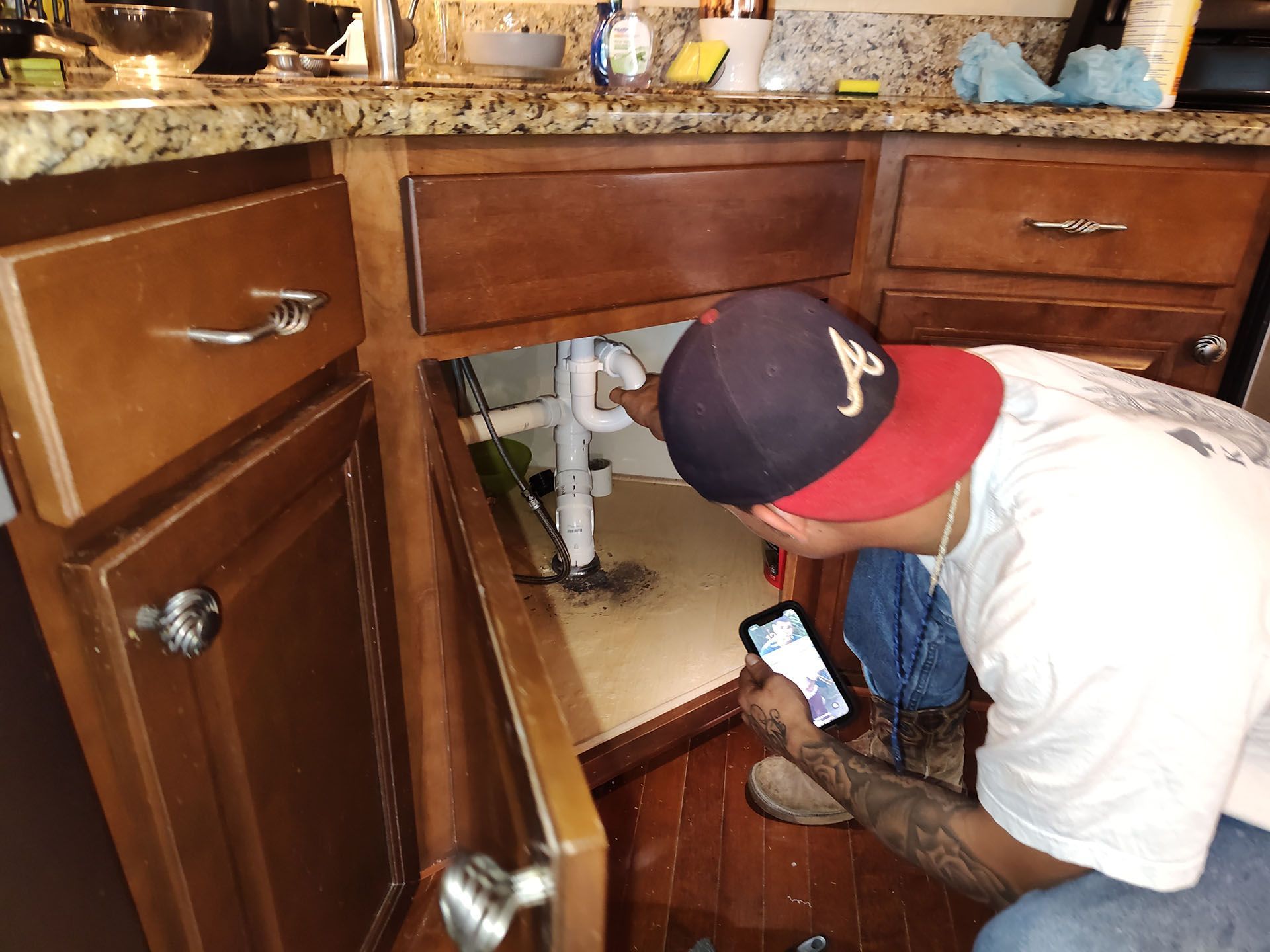 A man is looking under a sink in a kitchen.