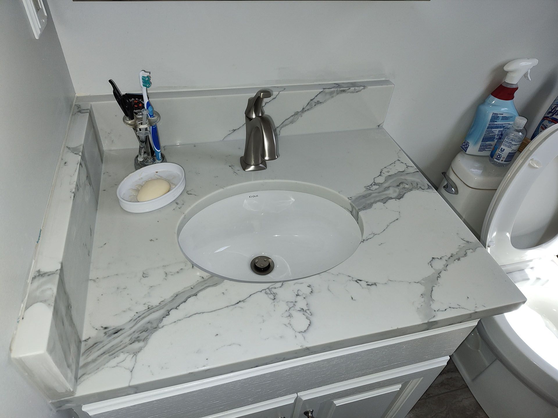 A bathroom sink with a marble counter top next to a toilet.