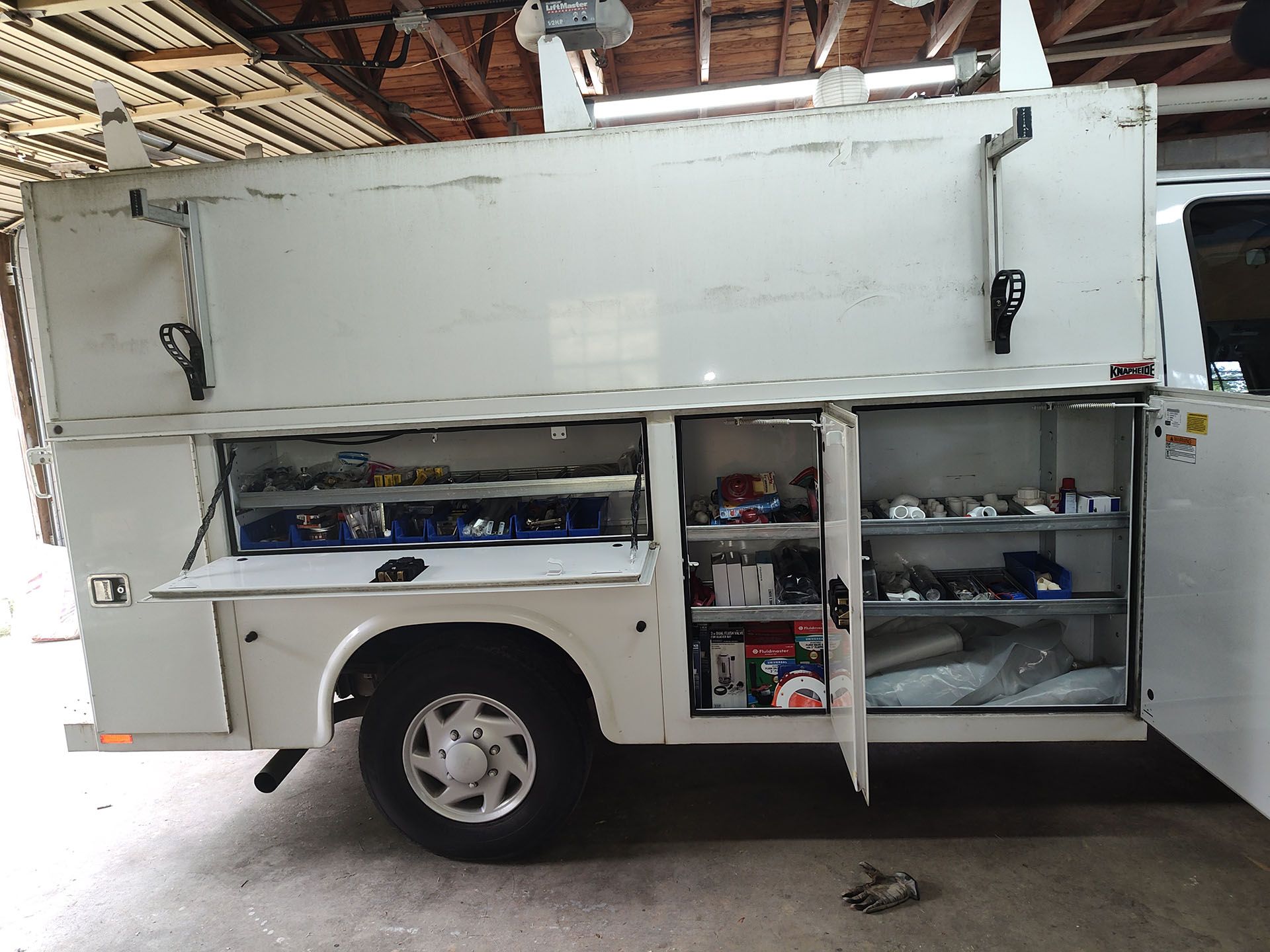 A white utility truck is parked with its doors open