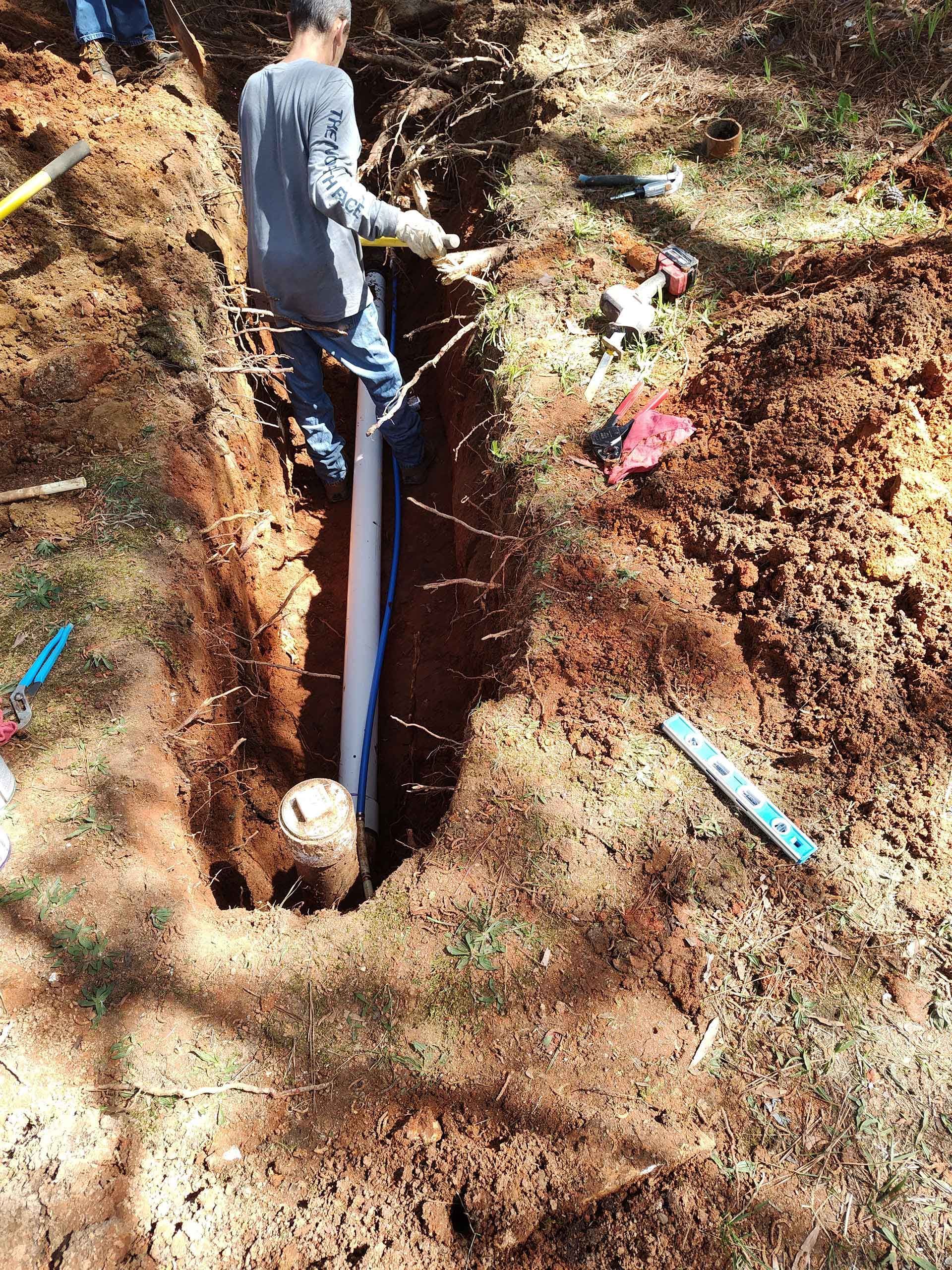 A man is digging a hole in the ground to install a pipe.