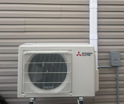 Mitsubishi Electric heat pump mounted on a building's siding, next to conduit and electrical box.