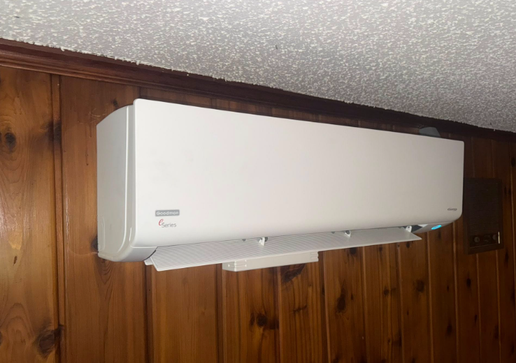 White air conditioner mounted on a wood-paneled wall, near a white ceiling.