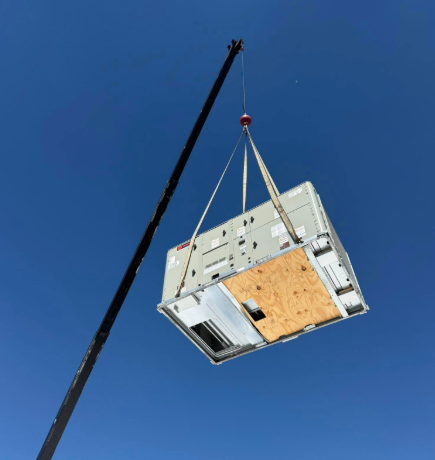 Crane lifting a large HVAC unit against a clear blue sky.