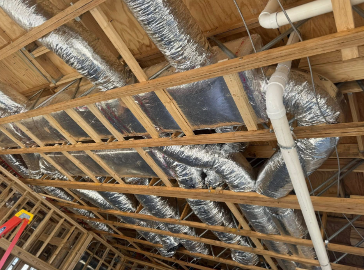 HVAC ductwork and plumbing pipes installed in a wooden attic frame.