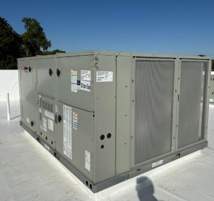 Large, gray rooftop HVAC unit on a white roof against a blue sky.