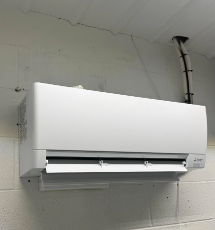White air conditioner unit mounted on a gray concrete wall with connecting pipes.