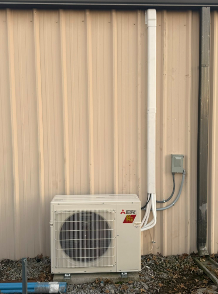 Mitsubishi air conditioning unit mounted on a beige building with white conduit.