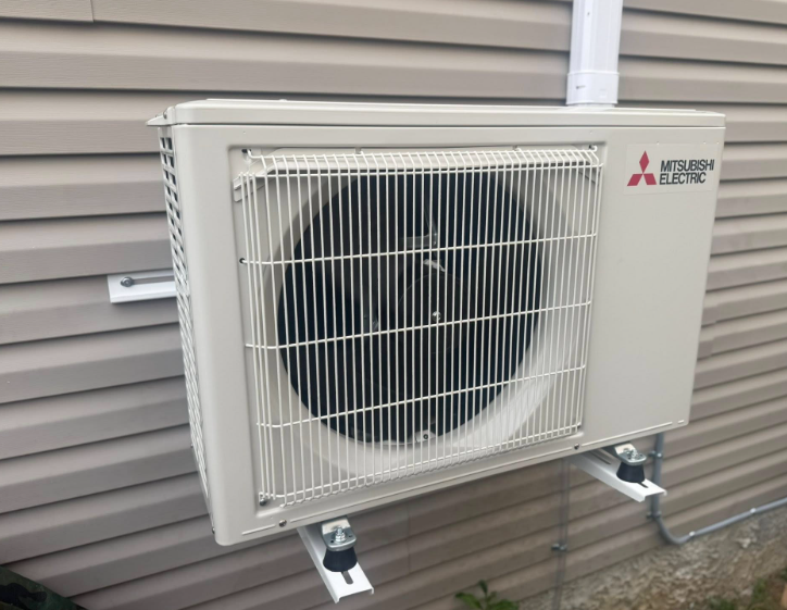 Mitsubishi air conditioner unit mounted on a beige house exterior.