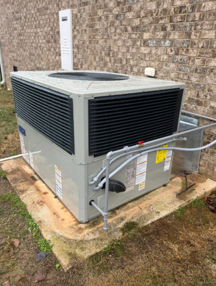 HVAC unit on a concrete pad outside a brick building. Gray metal, black grates, and white piping.