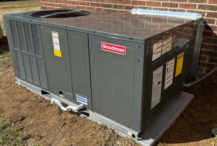 Dark gray Goodman air conditioning unit on a concrete pad next to a brick building.