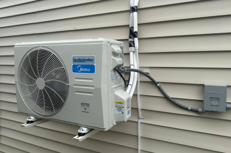 Midea air conditioner unit mounted on a beige siding wall, with electrical conduit and a gray junction box.