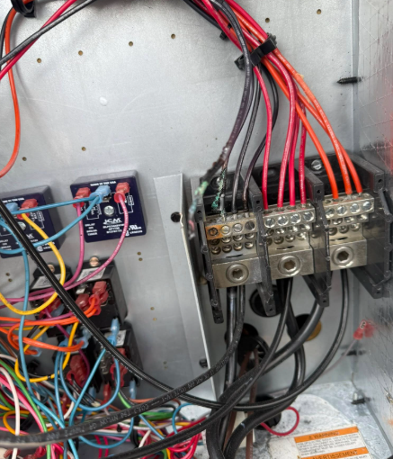 Electrical wiring and terminals inside a metallic HVAC unit. Wires are red, black, and blue.
