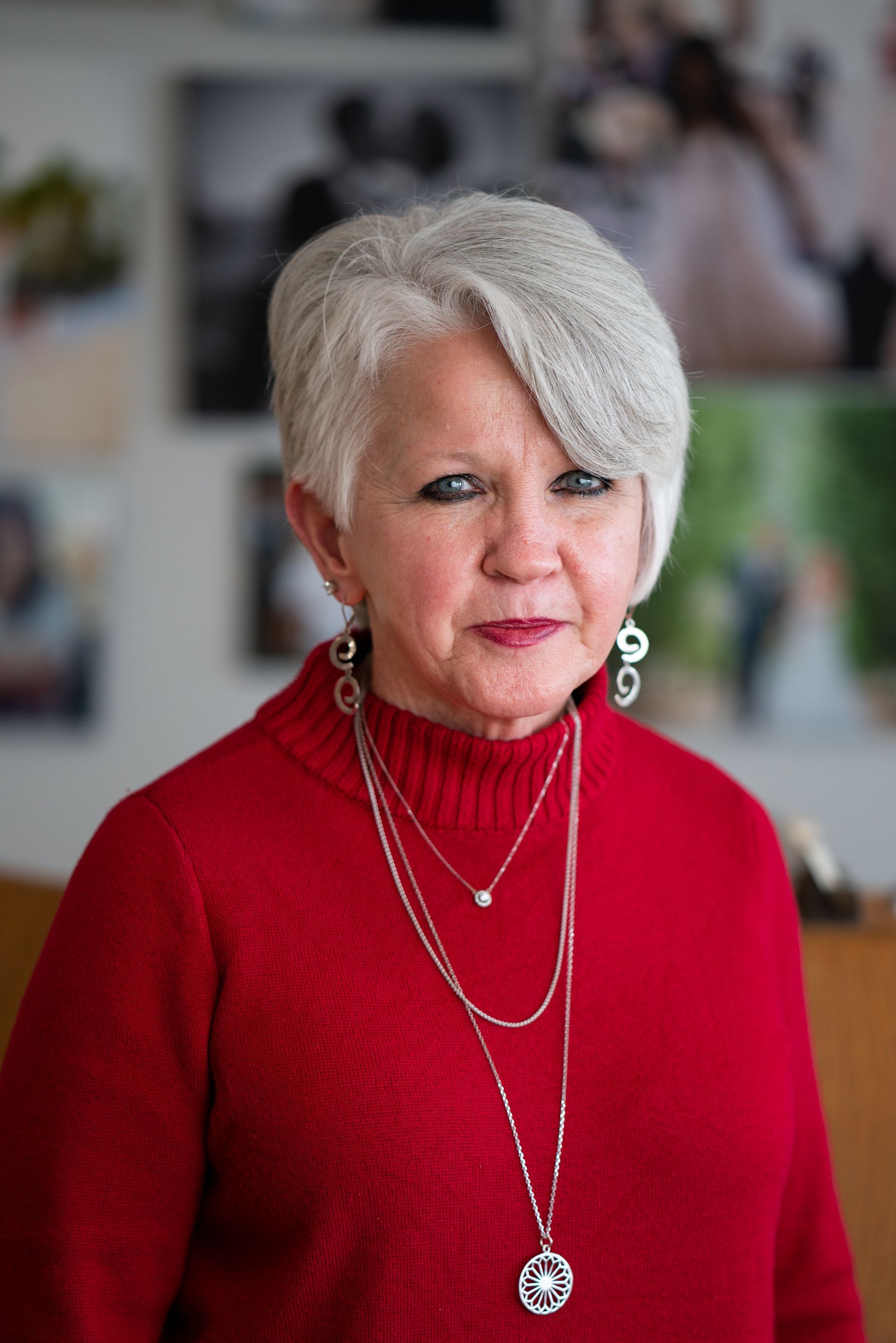 Portrait of a woman in a red top with silver jewelry, standing before a softly blurred indoor background