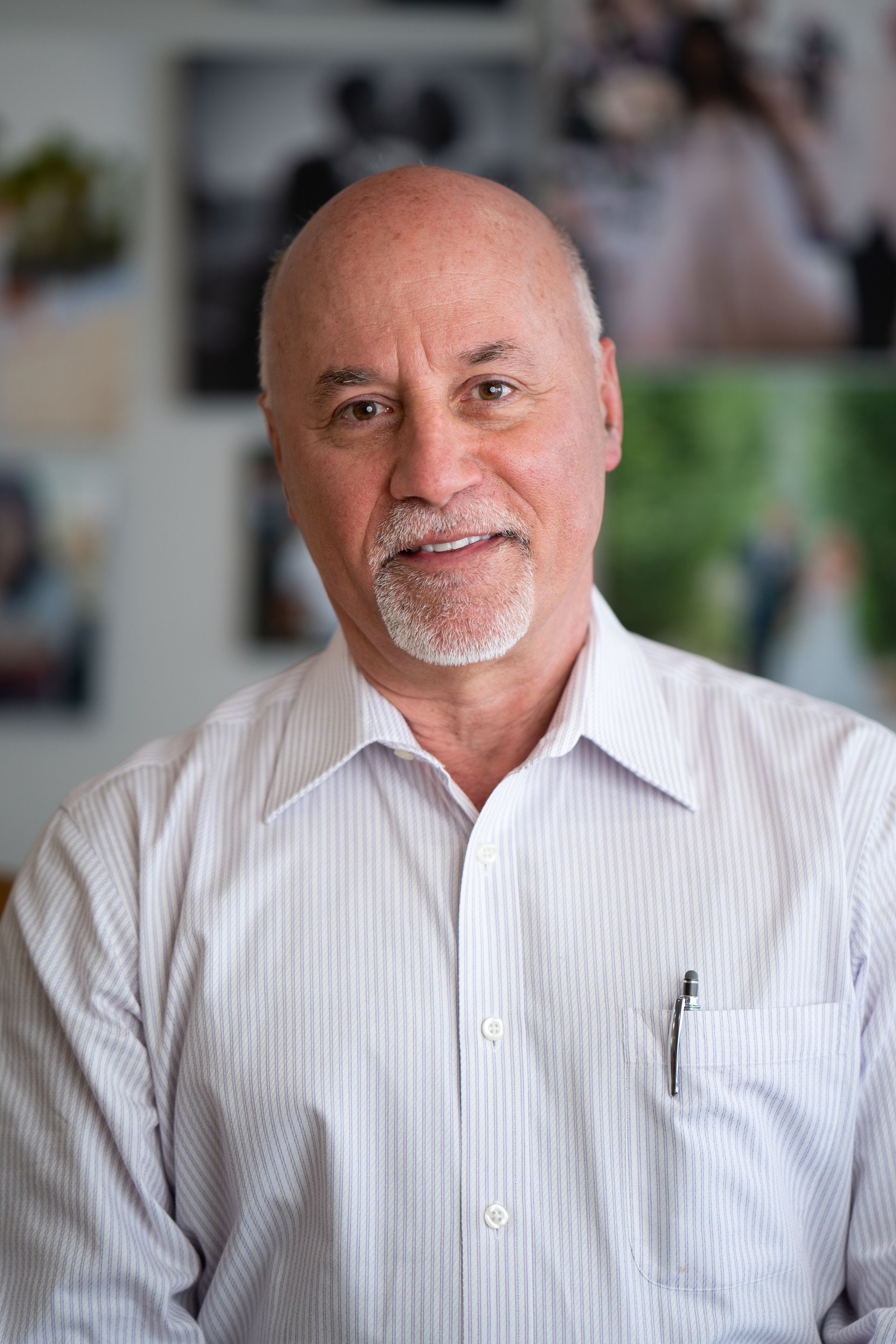 Portrait of a bald man in a white striped shirt, smiling softly against a blurred indoor background