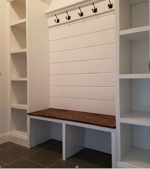 A hallway with a bench , shelves and hooks on the wall.