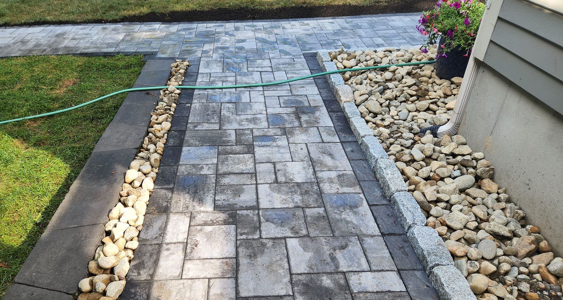 a brick walkway leading to a house with a hose attached to it