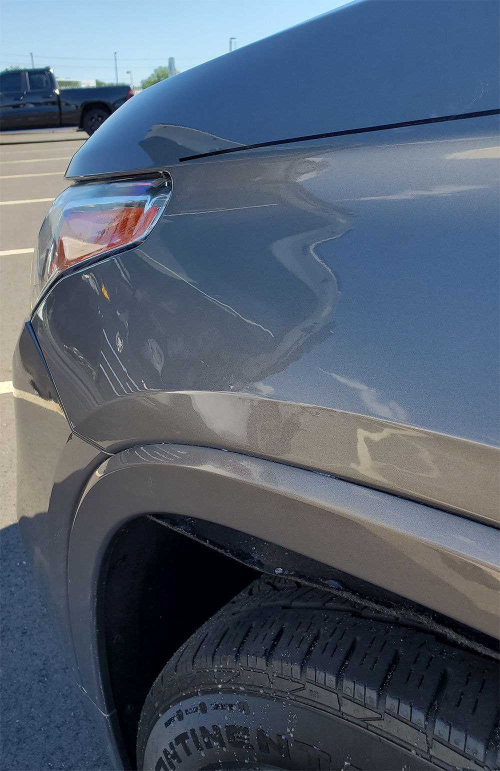 Close-up of a gray car’s front fender and headlight with visible scratches near the wheel arch