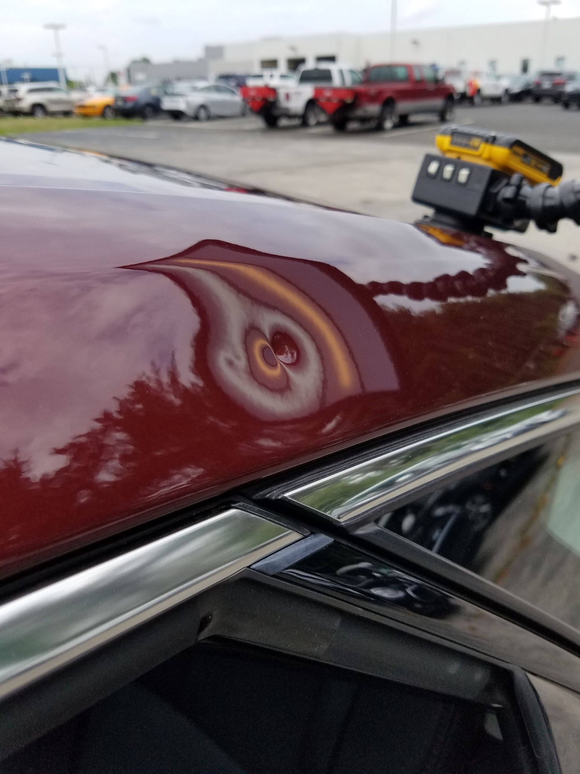 Close-up of a maroon car roof with a dent and chipped paint at a car lot.
