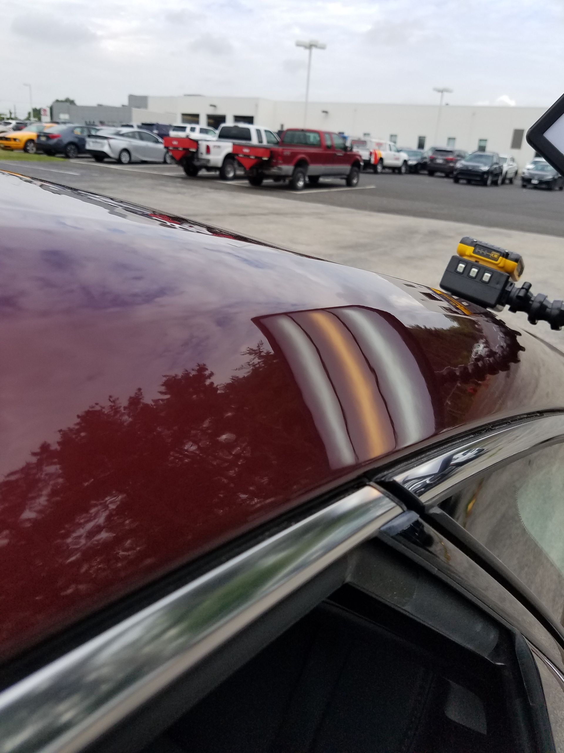 Close-up of maroon car hood with a reflective stripe in a parking lot