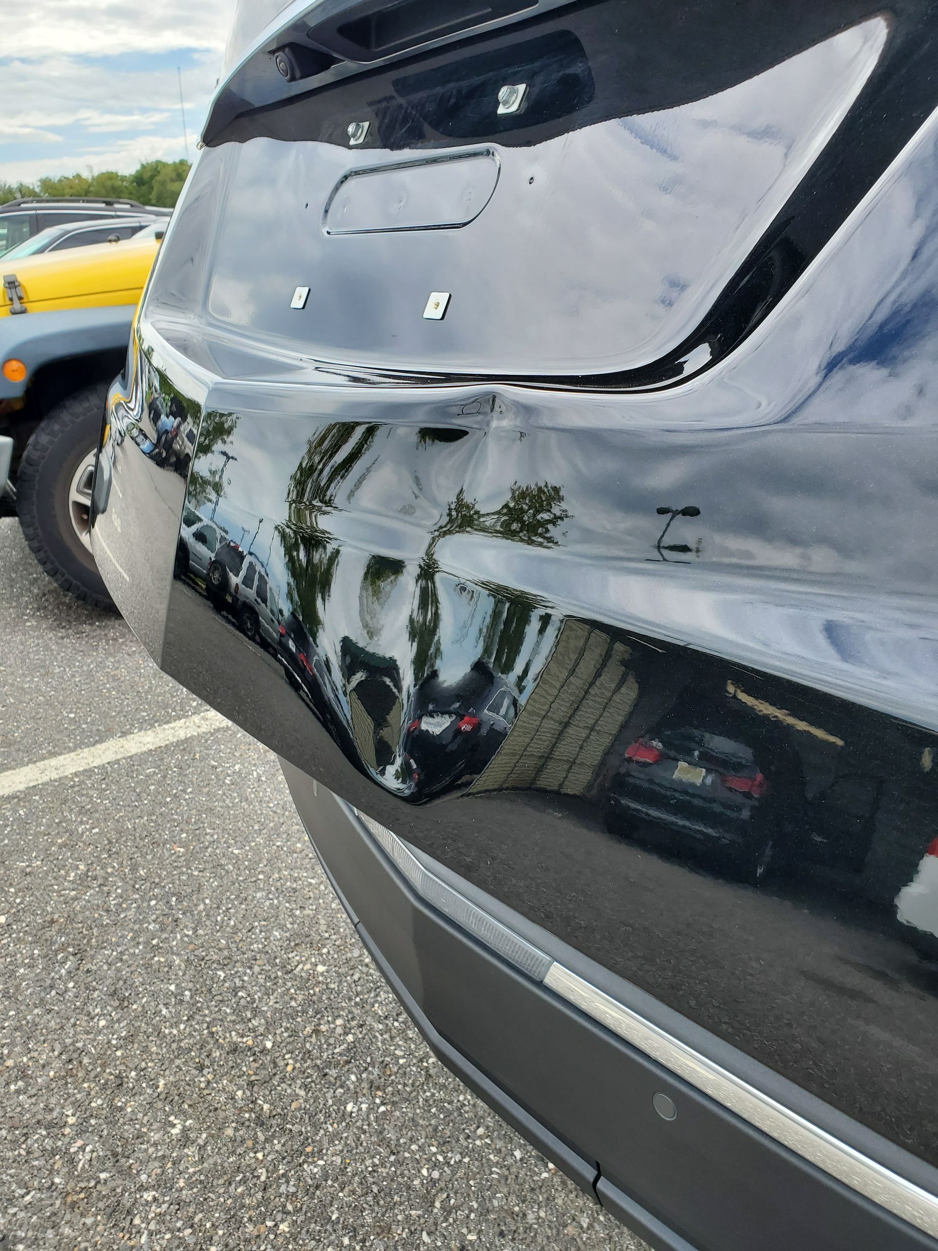 Close-up of a black SUV’s dented rear bumper with white scrape marks in a parking lot