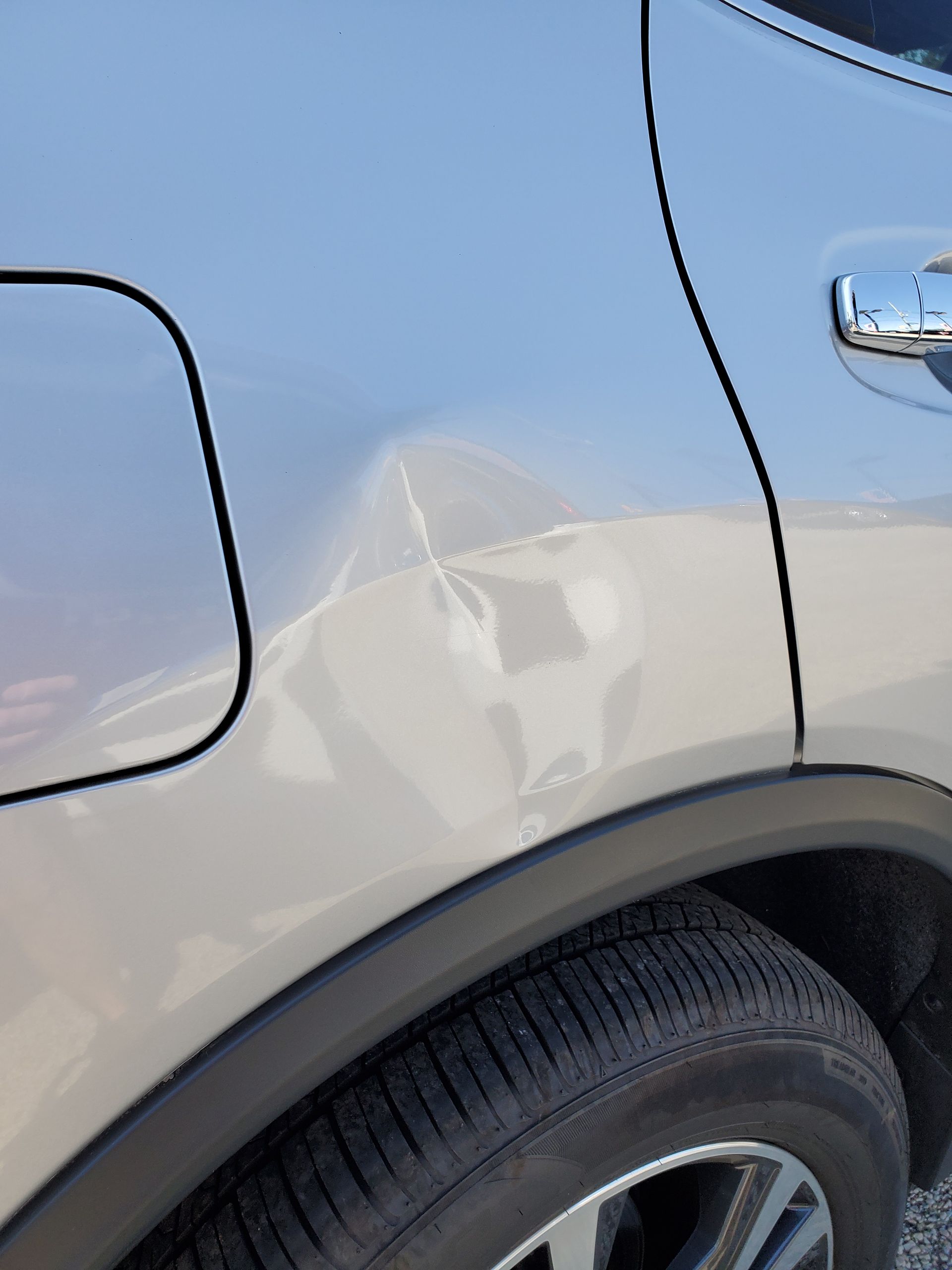 Close-up of a silver car’s rear side with a dented panel above the wheel arch.