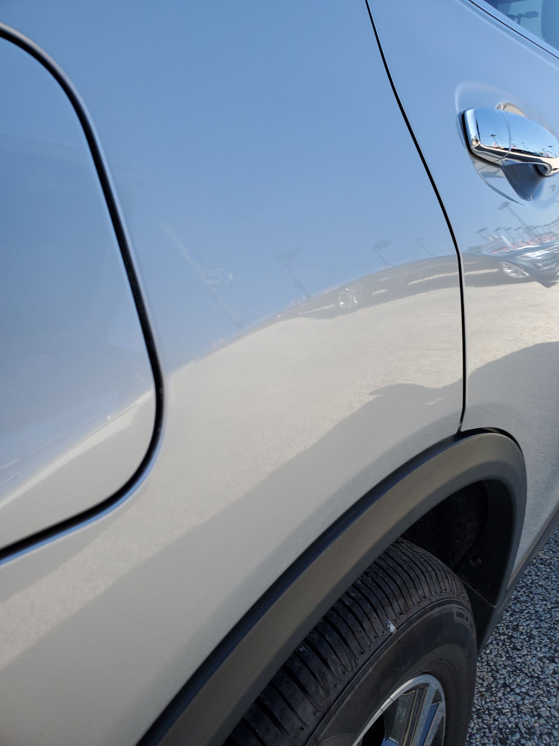 Close-up of a silver car’s side door, handle, and rear wheel in sunlight