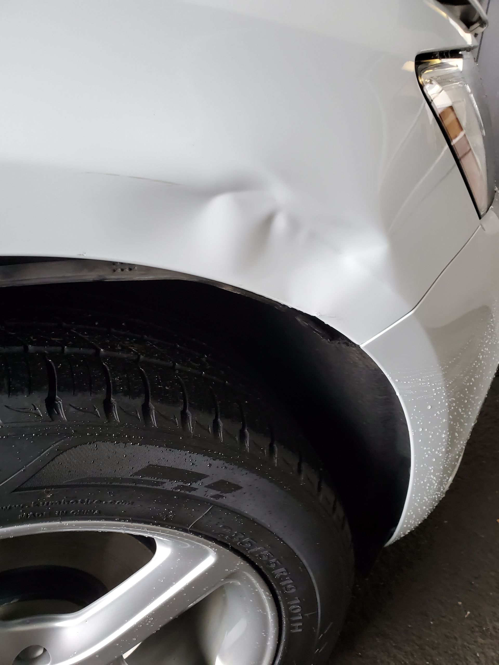 Close-up of a silver car’s front wheel and dented fender with visible body damage