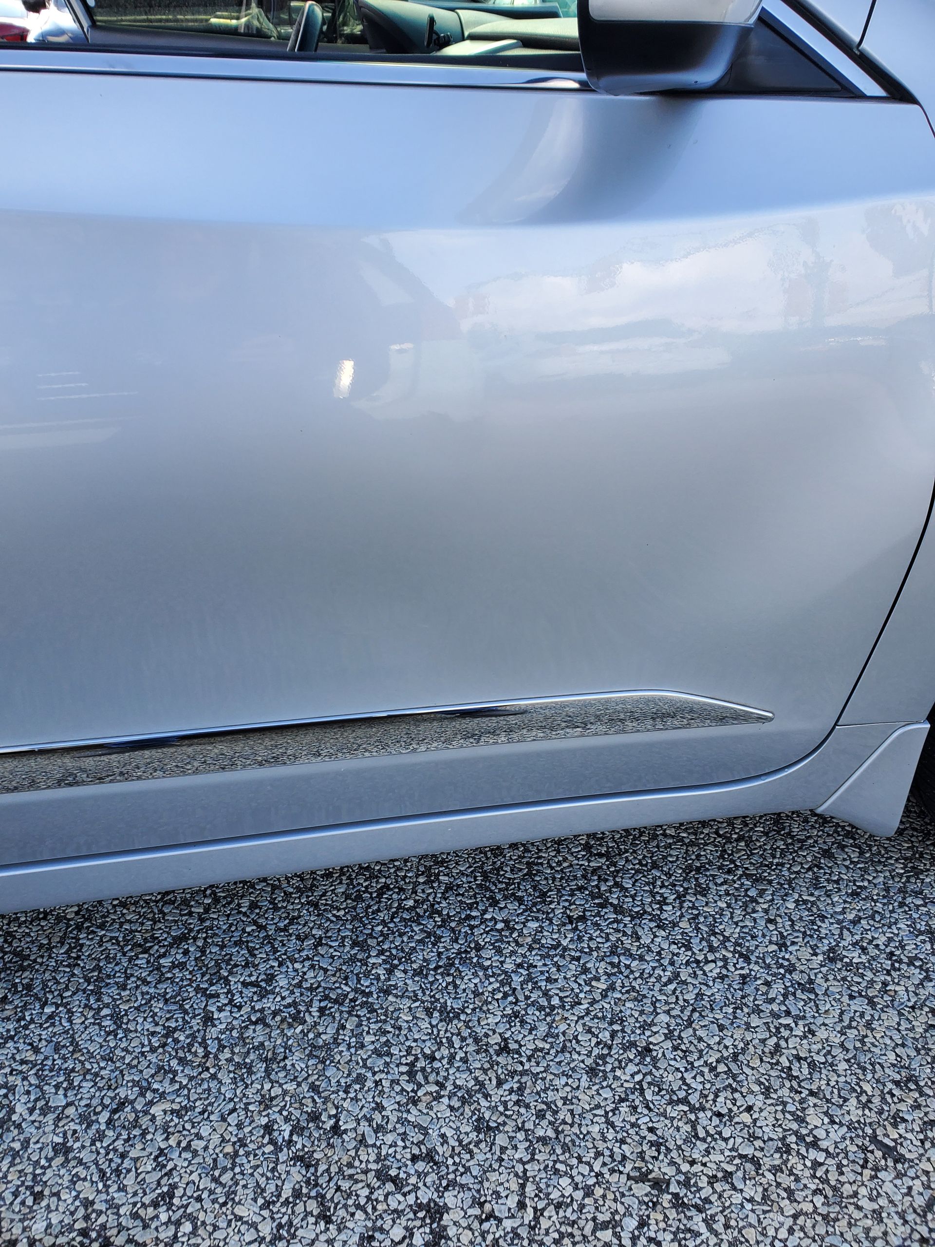 Close-up of a silver car door with a long scrape and chipped paint along the lower edge.