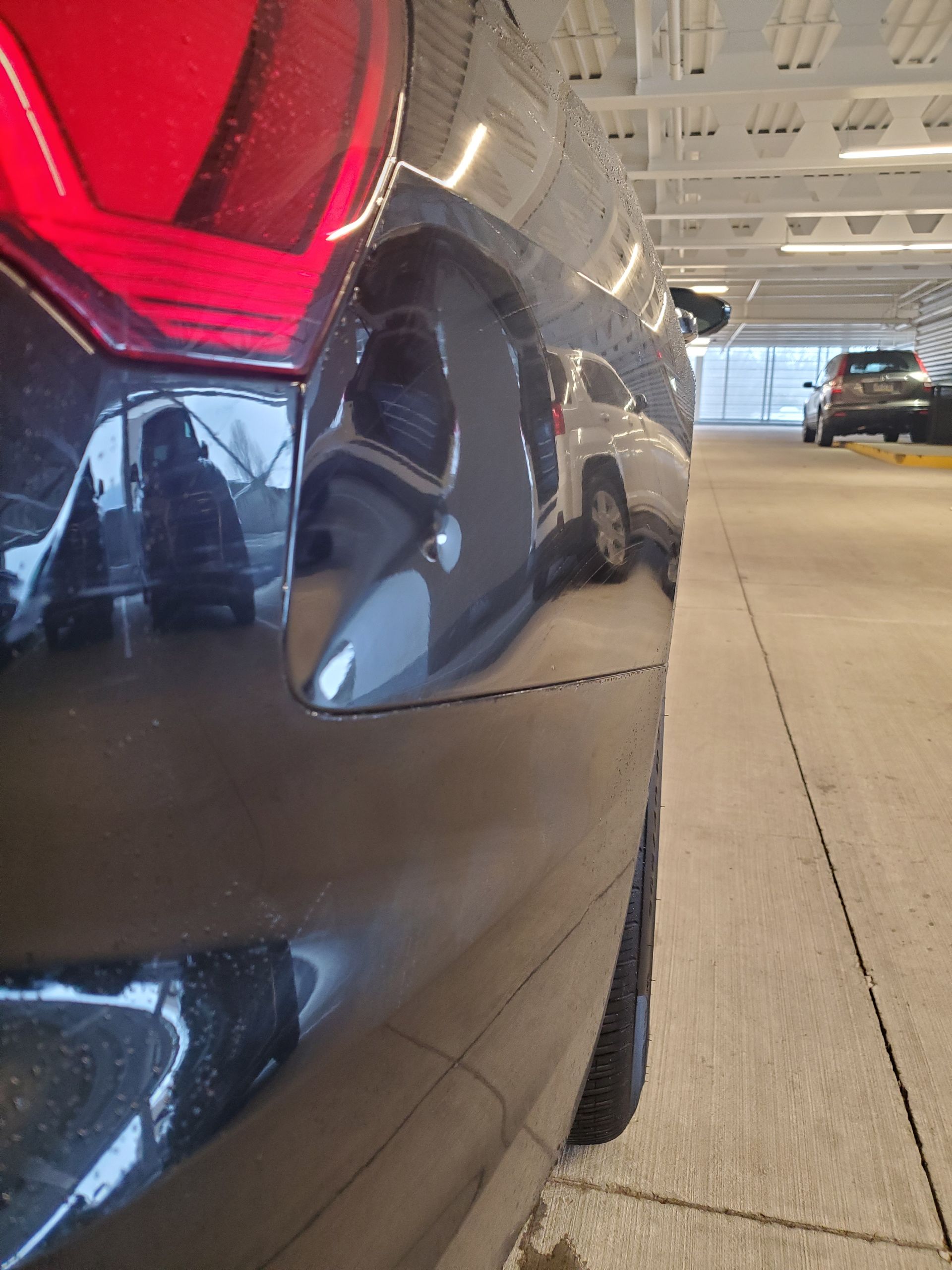 Close-up of a black car’s rear bumper and taillight in a parking garage
