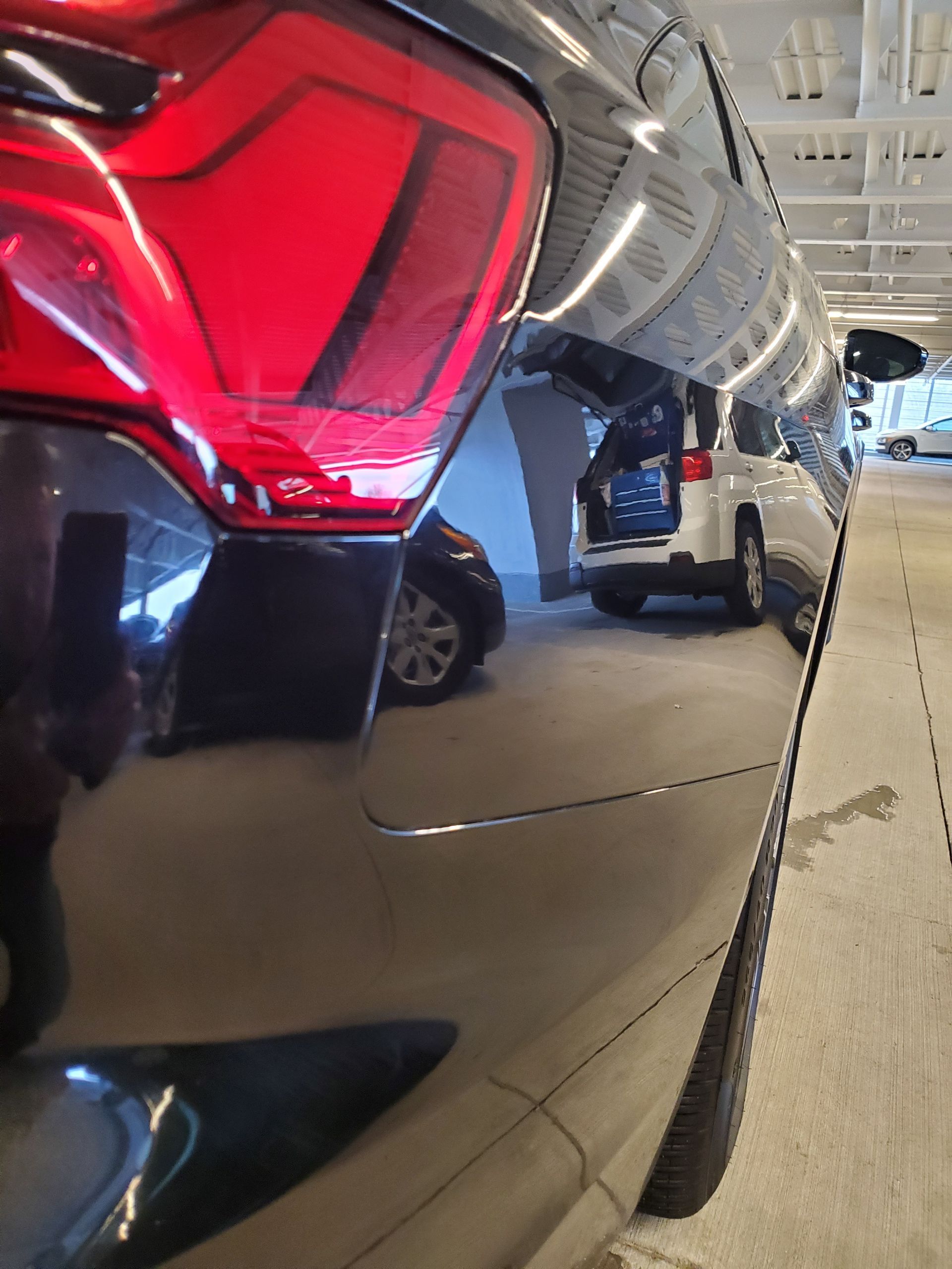 Close-up of a red SUV tail light in a parking garage, with car reflections on the glossy body.