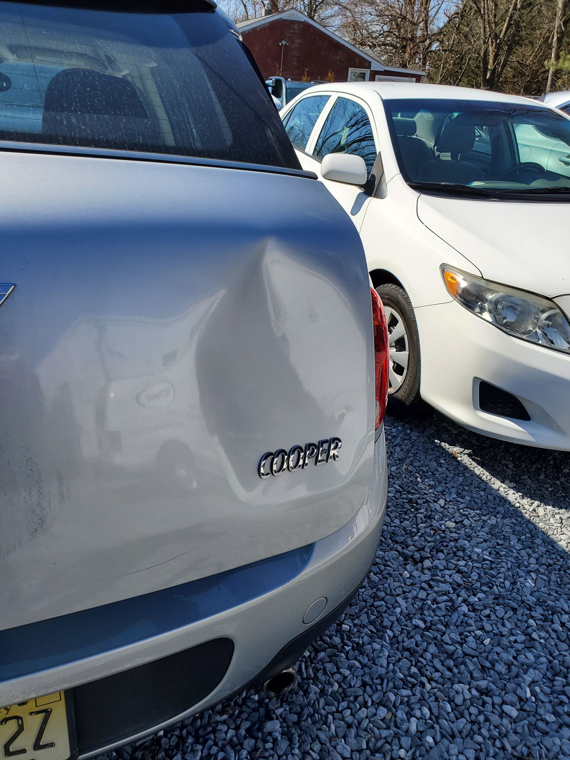 White car parked in a lot, close-up of rear badge, with another white car beside it in sunlight